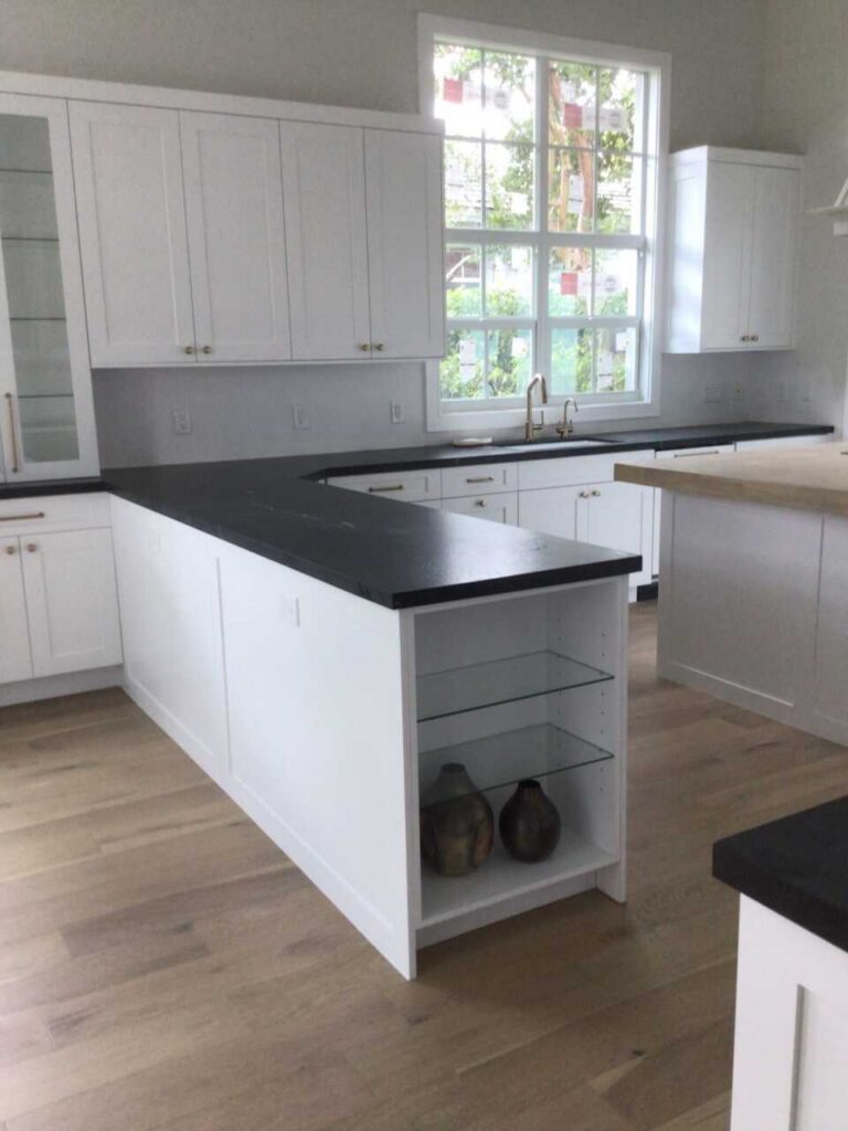 Modern kitchen with white cabinets, black countertops, and a large window above the sink.