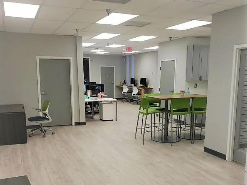 Modern office space with desks, computers, and green chairs around a high table.