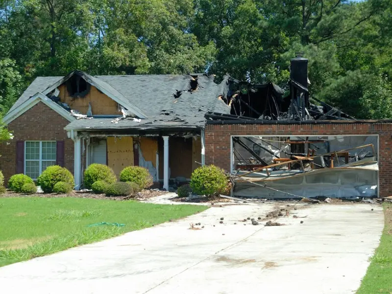 House with severe fire damage, including a collapsed garage door and charred roof.