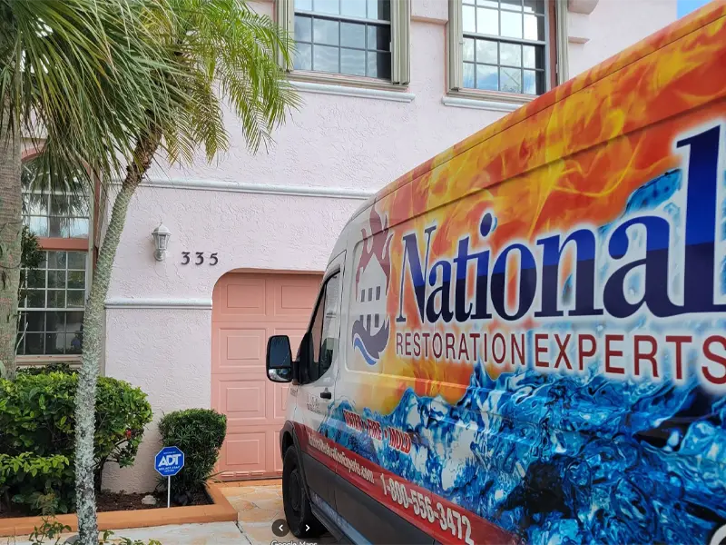A colorful National Restoration Experts van parked in front of a pink house with the number 335.