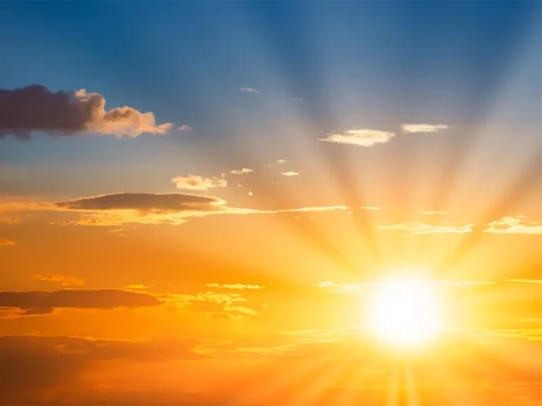 Bright sun rays shining through scattered clouds in a colorful sky at sunrise or sunset.