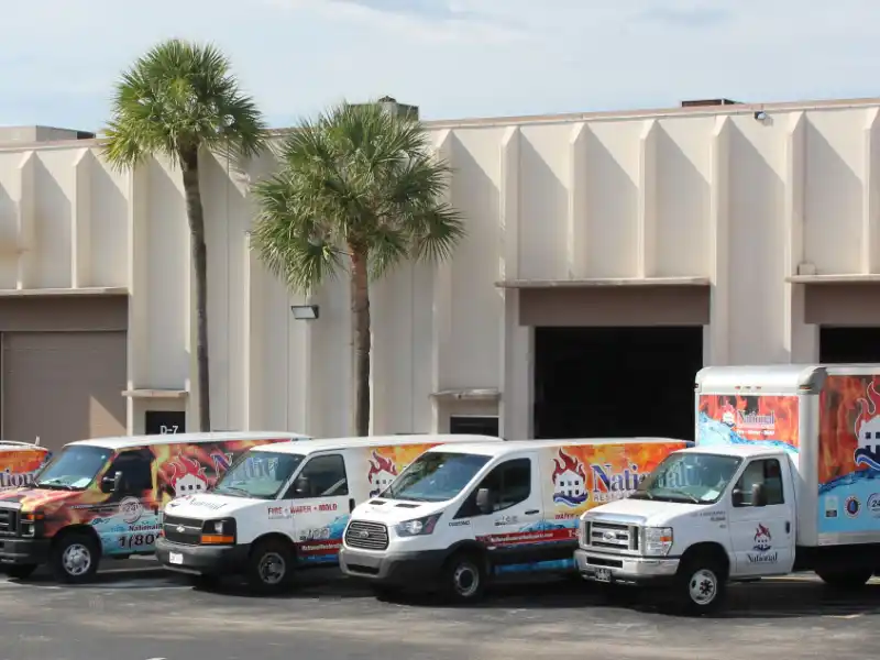 Four service vans with colorful flame-themed branding parked in front of a beige industrial building.